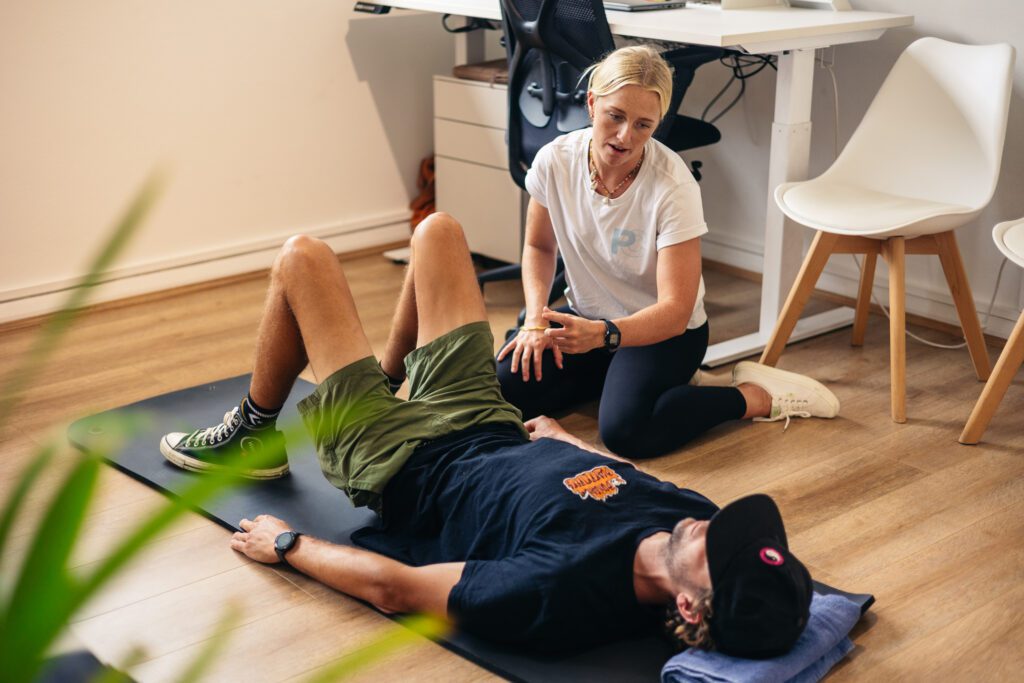 Female chiropractor talking to male patient lying on floor on yoga mat.