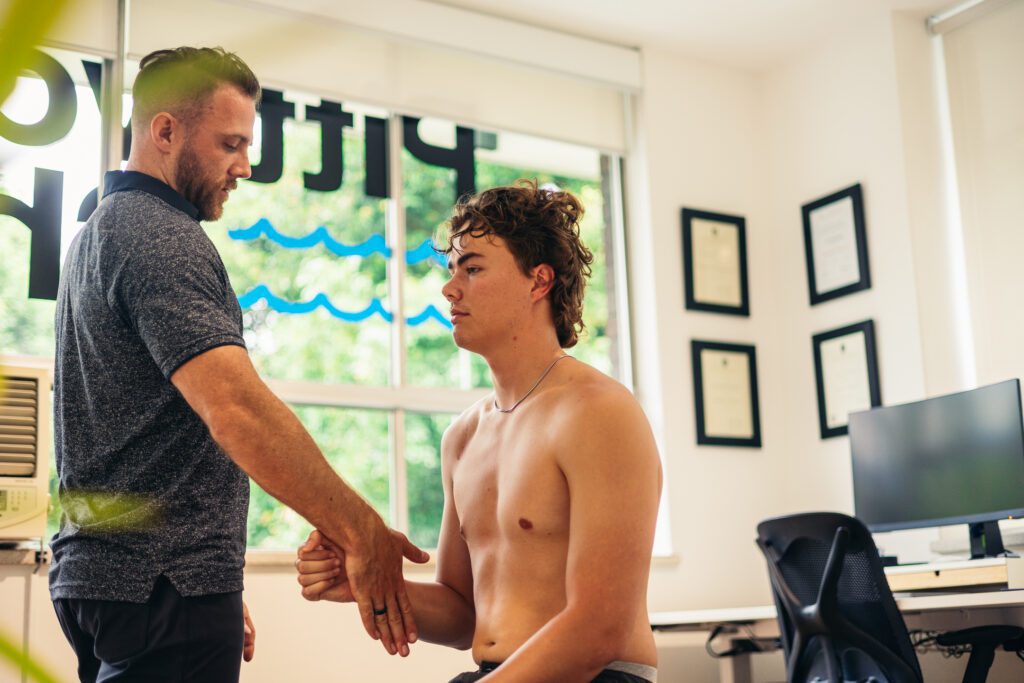 Male chiropractor assessing the shoulder strength of a male patient