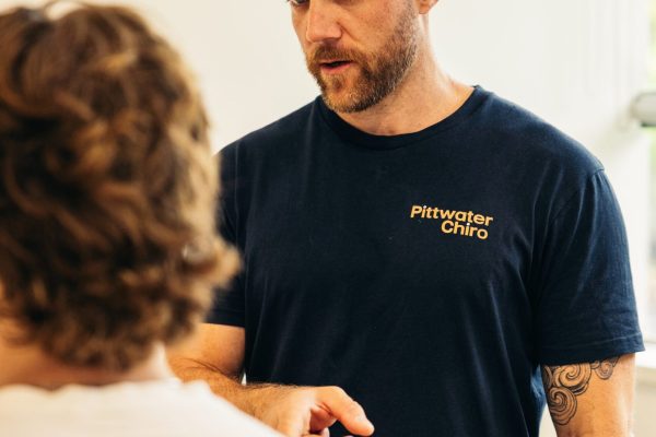Male chiropractor explaining pain in shoulder while male patient is seated.